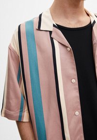 Camicia a maniche corte nei colori rosa chiaro, teal, crema e blu navy a righe, con colletto a camicia e bottoni beige, caratterizzata da una texture di tessuto liscia.
