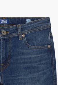 Tmavě modré džíny z denimu s kontrastním šitím, designem s pěti kapsami a kovovými knoflíky. Štítek na pasu nese nápis "JACK & JONES."