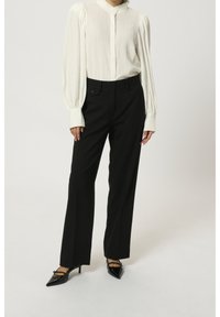 Witte, gestructureerde blouse met een hoge kraag en lange, geraffineerde mouwen; gecombineerd met zwarte, op maat gemaakte broeken en zwarte, puntige hakken.