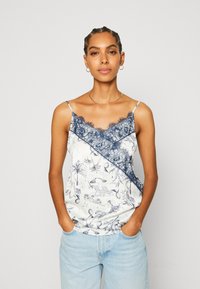 Top de tirantes en blanco con patrón floral azul, con borde de encaje azul con forma de ola en el escote, tirantes ajustables, tela ligera.