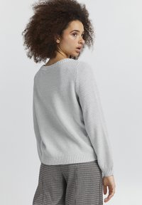 Hellgrauer Strickpullover mit einem strukturierten Muster, Rundhalsausschnitt und gerippten Bündchen, kombiniert mit karierten Hosen.