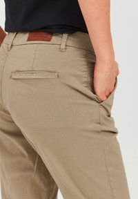 Pantaloni khaki realizzati in tessuto morbido con taglio dritto, dotati di una tasca posteriore e di un'etichetta in cuoio marrone apposta sulla vita.