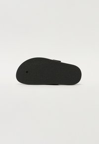 Sandal nera con suola in gomma texturizzata. Presenta una forma arrotondata e una singola cinghia regolabile sopra il piede per comfort e vestibilità.