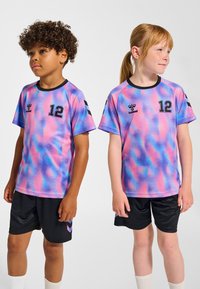 Två barn bär kortärmade, flerfärgade tie-dye fotbollströjor med svarta detaljer, siffror och shorts. Tyget verkar vara lätt och slätt.