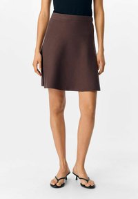 Jupe mini ajustée marron avec un design évasé et une texture lisse, dotée d'une taille cousue et d'un détail de fente sur le côté.