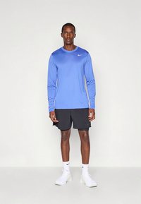 Nike långärmad blå träningsskjorta, svarta shorts och vita sneakers. Mjukt tyg, rund halsringning och subtil logodetalj.