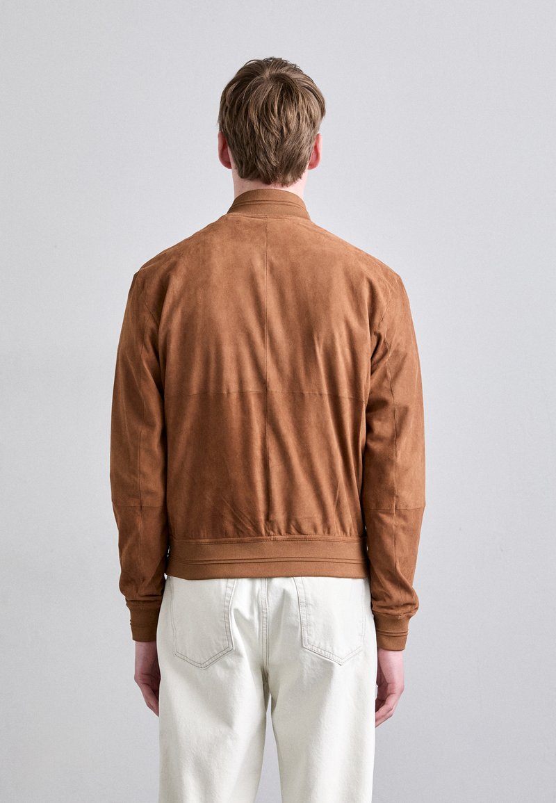 Chaqueta bomber de ante marrón con puños y dobladillo acanalados, con una textura suave y lisa. La vista trasera muestra un diseño ajustado y costuras mínimas.