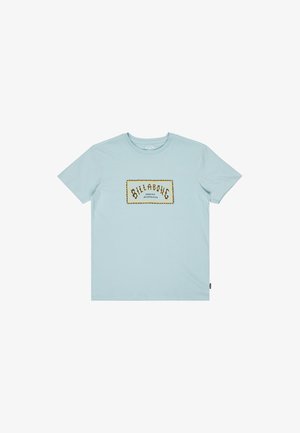 Lyseblå bomulds t-shirt med et rektangulært trykt label i guld og sort med teksten "BILLABONG" og "SINCE 1973". Klassisk rundhalsedesign.