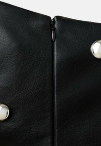 Čierna koženka s textúrovaným povrchom, so stredným zipsom a dvoma lesklými, guľatými kovovými gombíkmi.