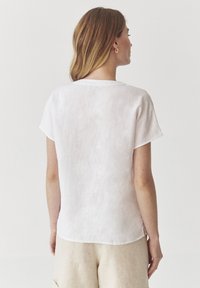 Kortærmet, lys pink linned top med rund halsudskæring, subtil tekstur og sideslidser. Bæres med lyse beige shorts.