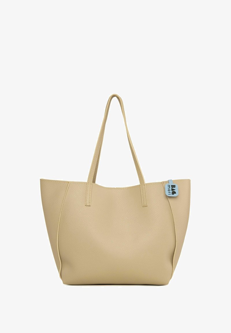 Beżowa torba typu tote o skórzanym, teksturowanym wykończeniu, z dwoma długimi uchwytami i prostokątnym kształtem, z niebieską metką jako akcentem po jednej stronie.