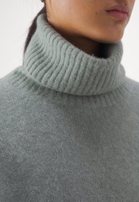 Hellgrüner Wollpullover mit Rollkragen und weicher Textur. Nahaufnahme, die die Details und die Verarbeitung des Stoffes zeigt.