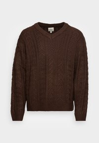 Pull marron en maille avec un col en V, présentant un motif torsadé texturé ainsi que des poignets et un ourlet côtelés, fabriqué en fil épais pour plus de chaleur.