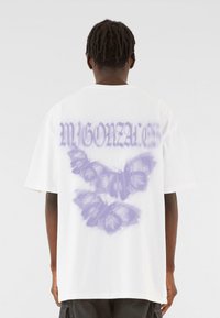 Hvid oversized t-shirt med et lilla sommerfugledesign og teksten "Mgonza" på ryggen. Korte ærmer og en afslappet pasform.