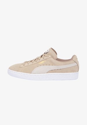 Jasnobeżowy zamszowy sneaker Puma z białą gumową podeszwą, beżowym paskiem Puma po boku, sznurowadłami i złotym logo Puma przy sznurowadłach.