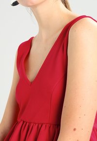 Abito rosso con profondo scollo a V, design senza maniche e gonna svasata. Tessuto morbido con una sottile trama.