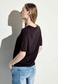 Černý top s krátkým rukávem a výstřihem do V, kombinovaný se světle modrými džíny. Materiál vypadá jemně a má volný střih.