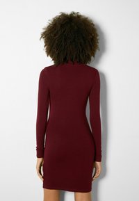 Burgundy långärmad kroppsnära klänning gjord av stretchigt material, med hög halsringning och midjehöjd. Enkel, sömlös design.