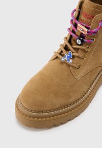 Stivale in suede beige con punta tonda, superficie testurizzata, suola in gomma a contrasto e lacci colorati con decorazioni a charms.