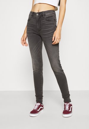 Jeans skinny grises de denim, con bolsillos frontales, cierre con botón y un ligero desgaste. Combinados con zapatillas burdeos.