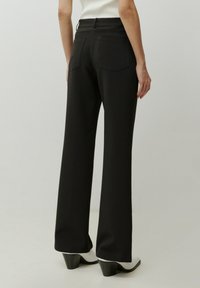 Zwarte wijde broek van een gladde stof, met twee achterzakken en strakke lijnen. Gecombineerd met witte enkelhakken.