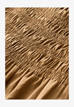 Brunt stof med rynket struktur og skiftende rækker, der skaber et bølget mønster. Blødt, let materiale falder glat.