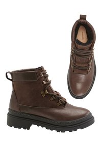 Botas de cuero marrón hasta el tobillo con suelas gruesas negras, cordones en la parte delantera con ojales metálicos, cuello acolchado y una lengüeta en la parte trasera, mostradas de lado y desde arriba.