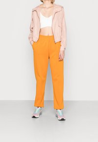 Ljusrosa zip-jacka med huva, vit croppad topp, orange sweatpants och mångfärgade sneakers. Snygga material, avslappnad passform och ren design.