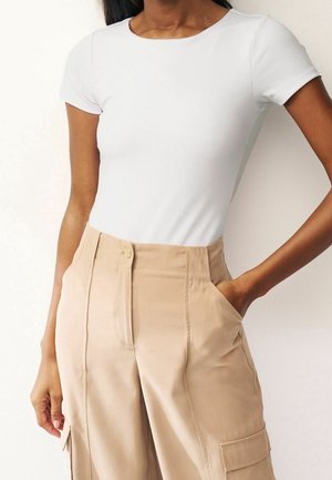 White fitted t-shirt with short sleeves, paired with beige high-waisted trousers featuring side pockets and a smooth texture.