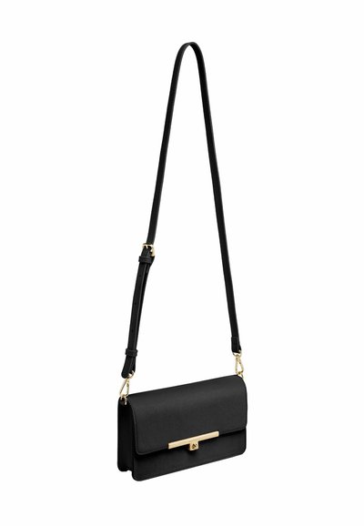 Črna usnjena torbica čez ramo z nastavljivim trakom in zlatim zapiranjem na sponko, visi na belem ozadju.