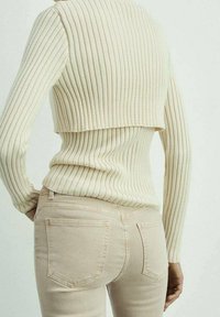 Suéter corto de punto acanalado en color crema con mangas largas, combinado con jeans ajustados de color beige claro que tienen dos bolsillos traseros.