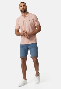 Ljusrosa pikétröja med krage och vita detaljer, i kombination med upprullade jeansshorts och vita sneakers. Enkel design, avslappnad passform.