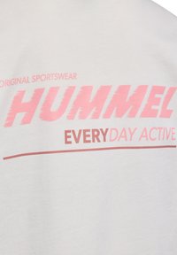Weißes Baumwoll-T-Shirt mit großen pinken Buchstaben, die "HUMMEL EVERY DAY ACTIVE" lesen. Das Design beinhaltet weiche, strukturierte Buchstaben mit einem sportlichen Look.