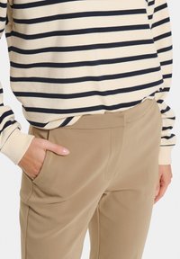 Haut à manches longues rayé en crème et marine, associé à un pantalon beige. Le haut présente des rayures horizontales ; le pantalon a une texture lisse avec des poches latérales.
