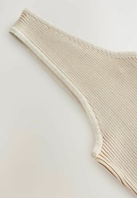 Beige ribota auduma stringi ar gludu tekstūru, ar plānu elastīgu joslu un šuvēm, kas nodrošina ciešu piegulšanu.