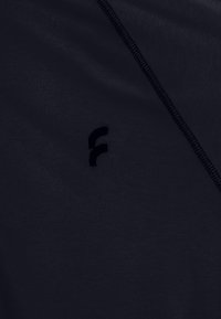 Top in tessuto navy con texture morbida, caratterizzato da un logo scuro discreto e cuciture piatte ai bordi. Il design è minimalista e slanciato.