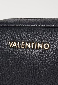 Svart texturerad läderväska med en guldig "VALENTINO"-logotyp. Designen inkluderar ett lockstängning och distinkt kornig yta.