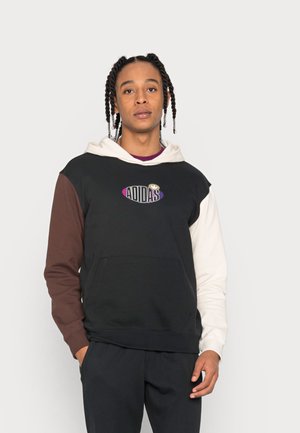 Hættetrøje med sort krop, brune og cremefarvede ærmer, forlommer og et farverigt Adidas-logo på brystet. Blød stoftekstur.