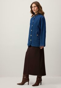 Tmavomodrá rifľová bunda so zlatými gombíkmi, dlhými rukávmi a bočnými vreckami. Kombinovaná s hnedou sukňou dĺžky po zem a hnedými topánkami.