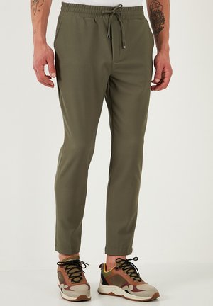 Pantalones deportivos verde oliva con cintura elástica, cordón ajustable y bolsillos laterales, combinados con zapatillas multicolores.