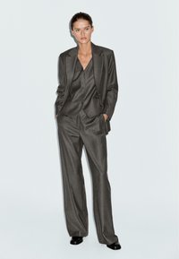 Completo tre pezzi grigio a righe sottili composto da un blazer aderente, un gilet e pantaloni a gamba larga; tessuto liscio con un design strutturato.
