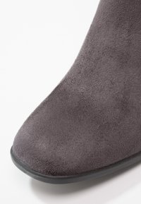 Bottine en daim gris avec un bout arrondi, texture lisse et une semelle en caoutchouc noire. Pas de quincaillerie ou de motifs visibles.