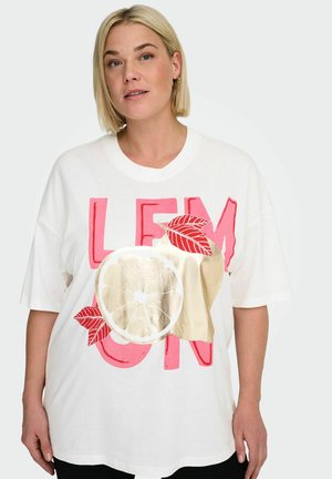 Lyshåret kvinde iført hvid, oversized T-shirt med rød tekst "LEMON" og grafik af citronskive, blade og cremefarvet abstrakt form.