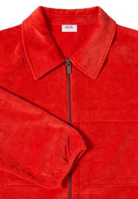 Červená manšestrová bunda s límcem a zapínáním na zip. Má žebrovanou texturu a elastické manžety, značková s visačkou "CECIL".