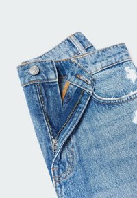 Jean en denim bleu clair avec braguette à glissière et bouton en métal. Présente des accents usés et des coutures contrastées.