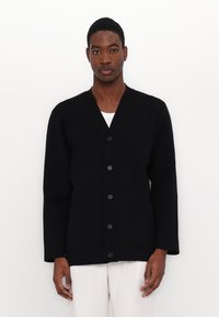 Cardigan noir avec un décolleté en V, fermeture à six boutons à l'avant et deux poches avant. Fabriqué en tissu texturé, avec des manches longues.