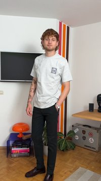 Gray cotton t-shirt with a graphic pocket design, paired with black slim-fit trousers and brown leather shoes. Indoor setting with decor.