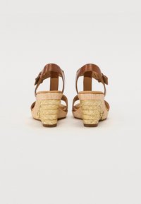 Brown leather strap sandals with woven, light tan heel and ankle buckle. Open back design with a textured woven surface on the heel.
