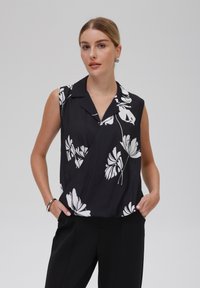 Top nero senza maniche con stampa floreale bianca, dotato di colletto e design asimmetrico. Tessuto morbido con una texture liscia.