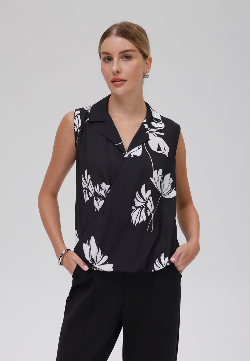Top nero senza maniche con stampa floreale bianca, dotato di colletto e design asimmetrico. Tessuto morbido con una texture liscia.